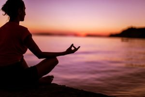 una ragazza medita in riva al mare al tramonto