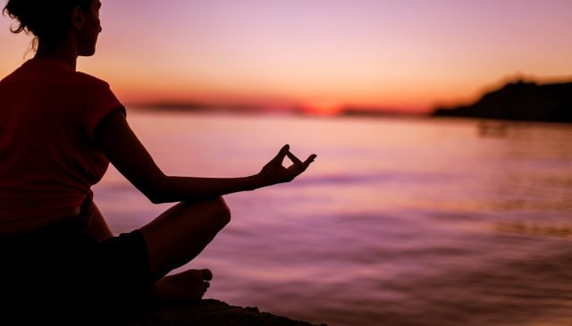 una ragazza medita in riva al mare al tramonto