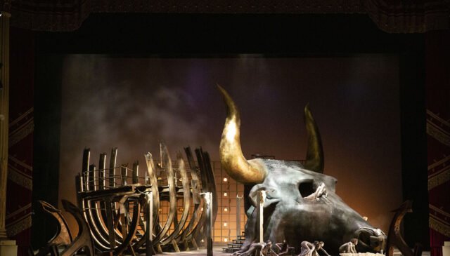 Al centro della scena unica troneggiano il relitto di una nave e la testa di un toro
