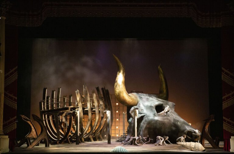 Al centro della scena unica troneggiano il relitto di una nave e la testa di un toro