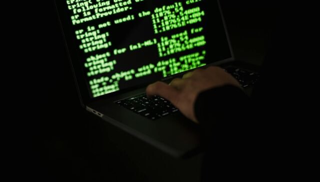 crop hacker typing on laptop with information on screen