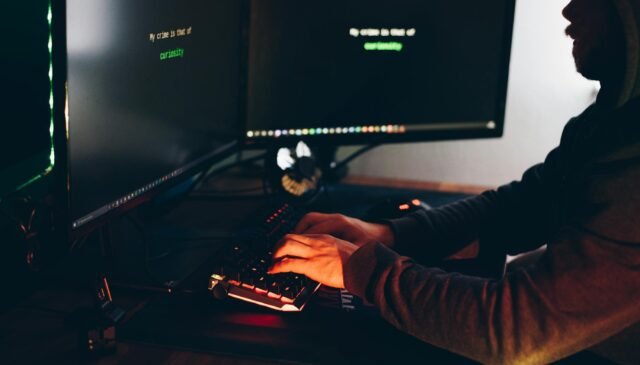crop hacker silhouette typing on computer keyboard while hacking system