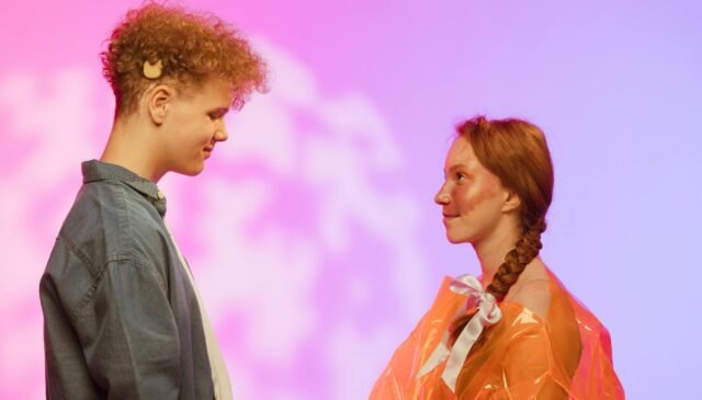 a man in denim shirt in front of a woman in orange plastic top