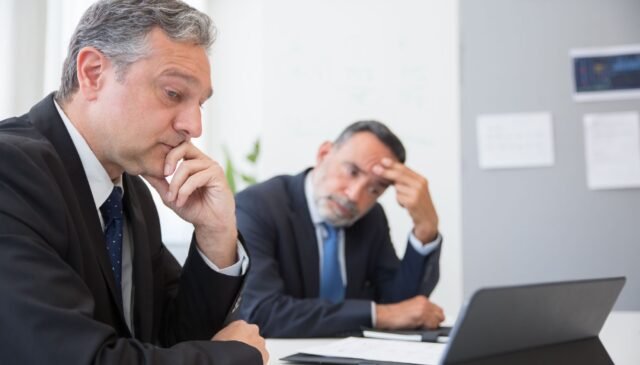 man in black suit jacket sitting beside man in black suit